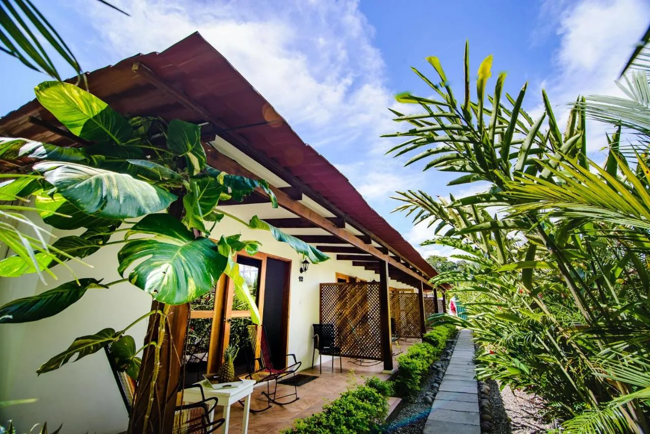 El corredor de las habitaciones: paredes blancas, techo rojo sobre vigas de madera y plantas tropicales.