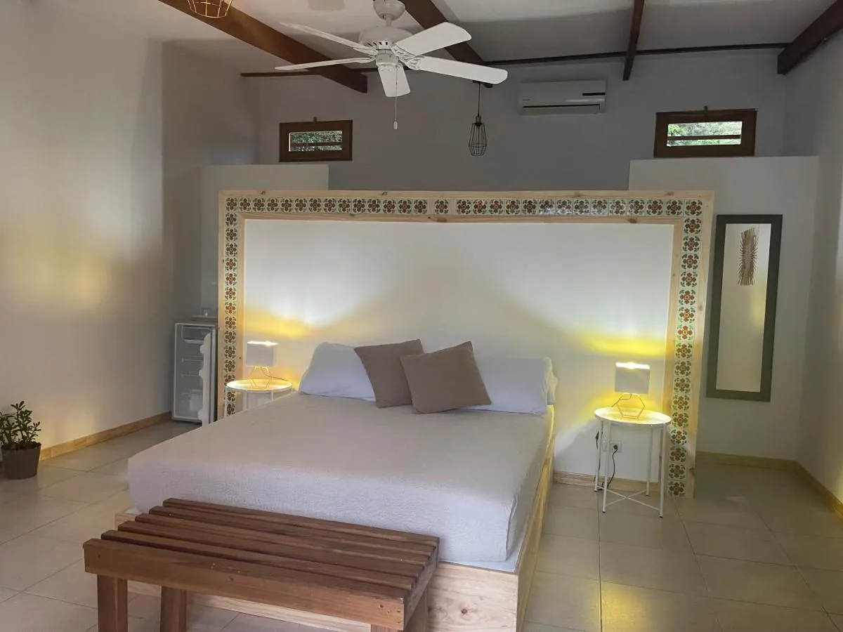 Cama doble con cabecero de pino enmarcado en azulejos, lámparas encendidas y ventilador de techo.