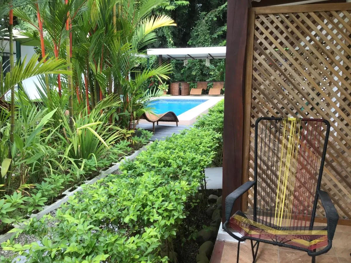 Terraza de una habitación con sillas de hilo de colores, celosía de madera y el jardín con la piscina al fondo.